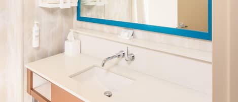 A modern bathroom with a large mirror, white sink, and neatly stacked towels.