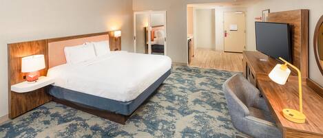Une chambre d’hôtel comprenant un lit, des lampes de chevet, un bureau avec une chaise, une télévision et un miroir.