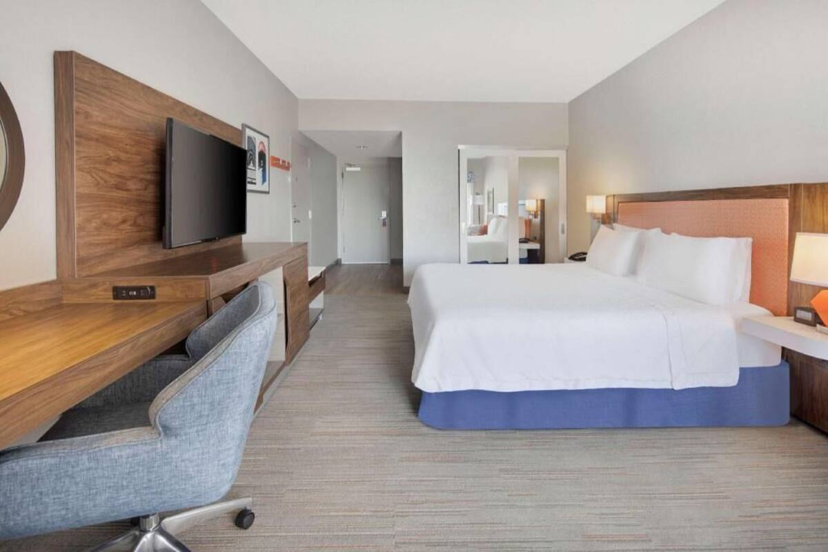 A hotel room with a bed, desk, chair, TV, and a mirror.