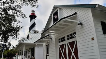 A white building with a black and red lighthouse, a covered porch, and a garage with red doors.