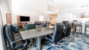 A conference room with a long table, several chairs, a television, and a painting on the wall.