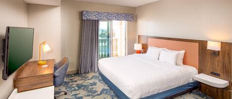 A hotel room with a large bed, a desk with a chair, a TV, and a window with curtains.