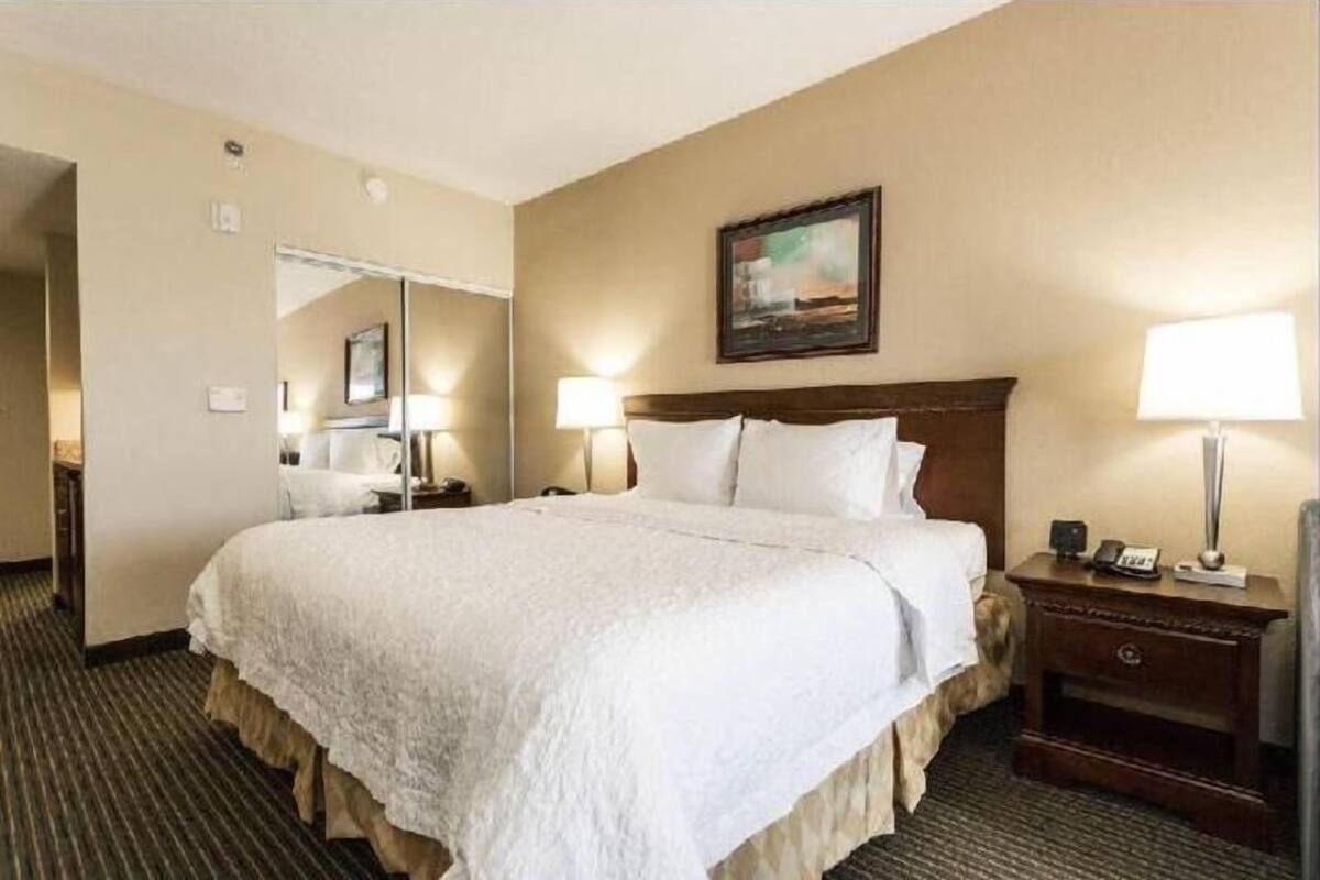 A hotel room with a large bed, a bedside table with a lamp, a mirror, and a painting on the wall.