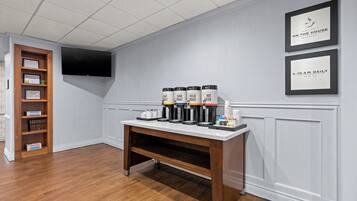 Camera d'albergo con angolo caffè in legno, una libreria e una TV a schermo piatto montata a parete.