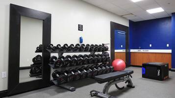 A gym with a bench, dumbbells, a red exercise ball, and a weight bench.
