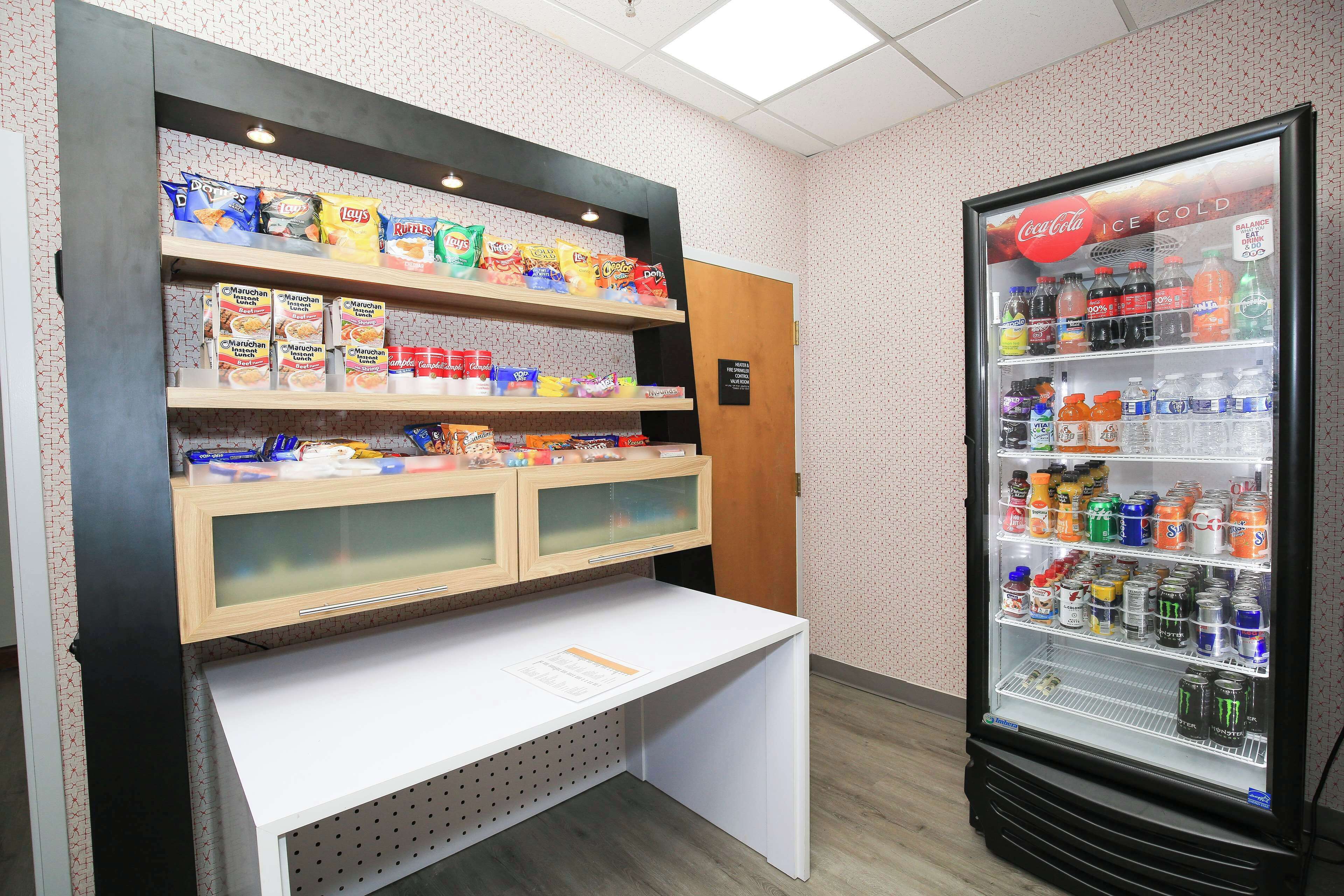 A vending machine stocked with snacks and beverages, a display of packaged goods, and a white counter with a menu.