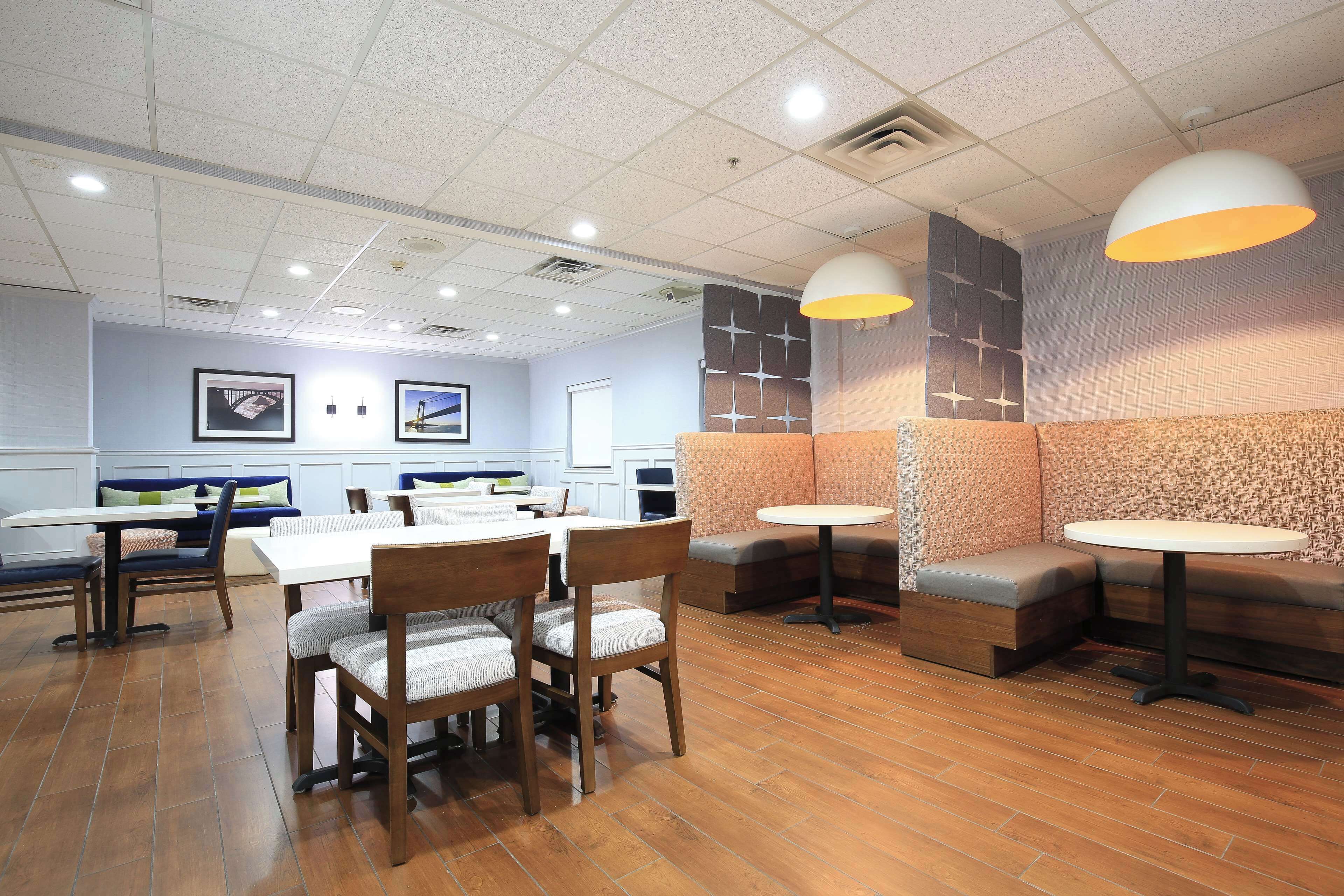 Un restaurante con mesas y sillas de madera, asientos acolchados e iluminación colgante.