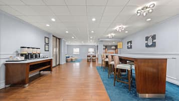 A spacious room with a wooden floor, a reception desk, a coffee station, and a seating area with chairs and a table.