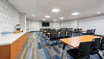 Un salón de conferencias con mesas, sillas, una pizarra y un mostrador con útiles.