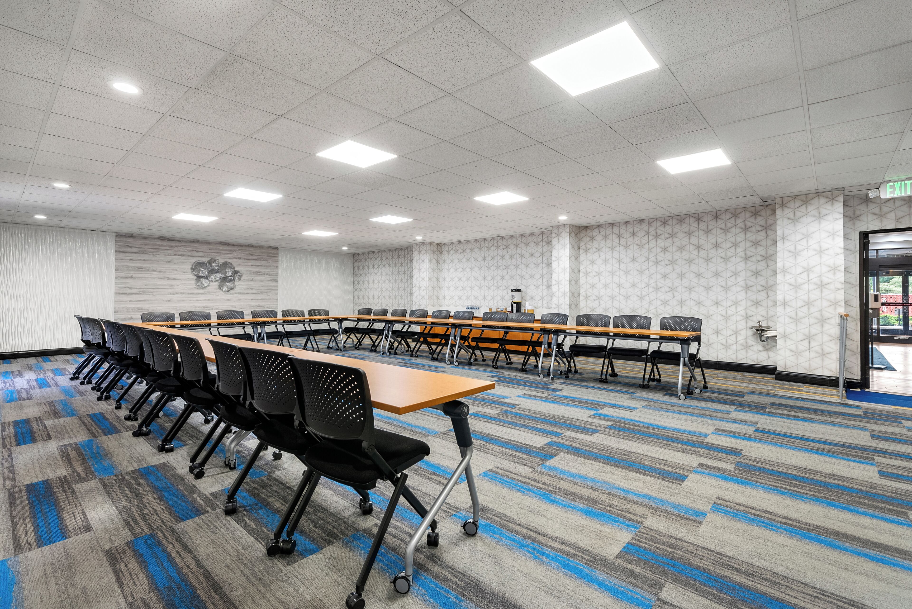 A conference room with a long table, multiple chairs, and a patterned carpet.