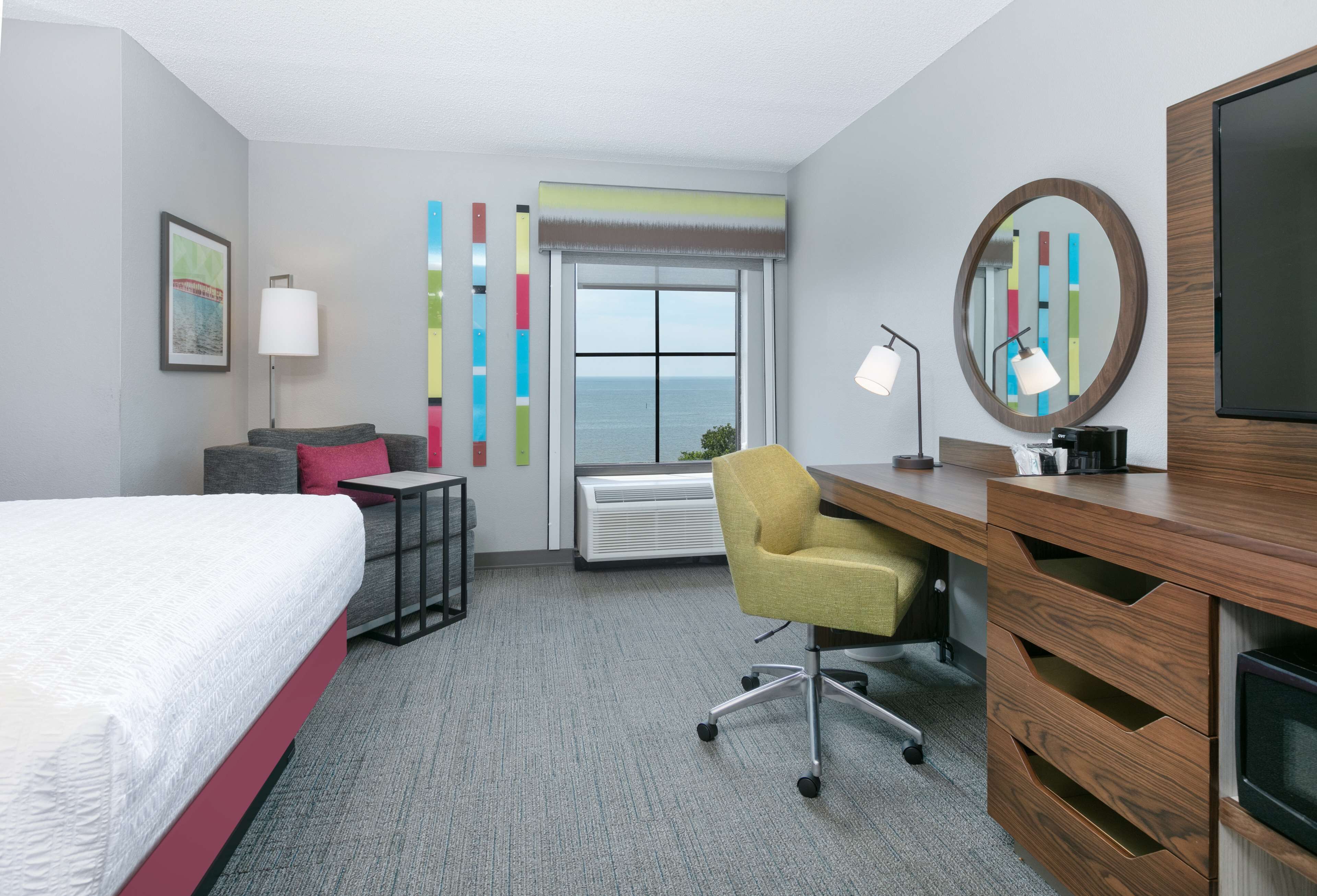 Une chambre d’hôtel équipée d’un lit, d’un bureau, d’une chaise et d’une grande fenêtre donnant sur la mer.