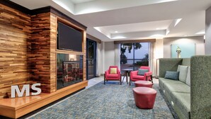 A modern hotel lobby with a wooden accent wall, a flat-screen TV, a fireplace, and a seating area with red and green upholstered furniture. - Hampton Inn Biloxi (Biloxi)