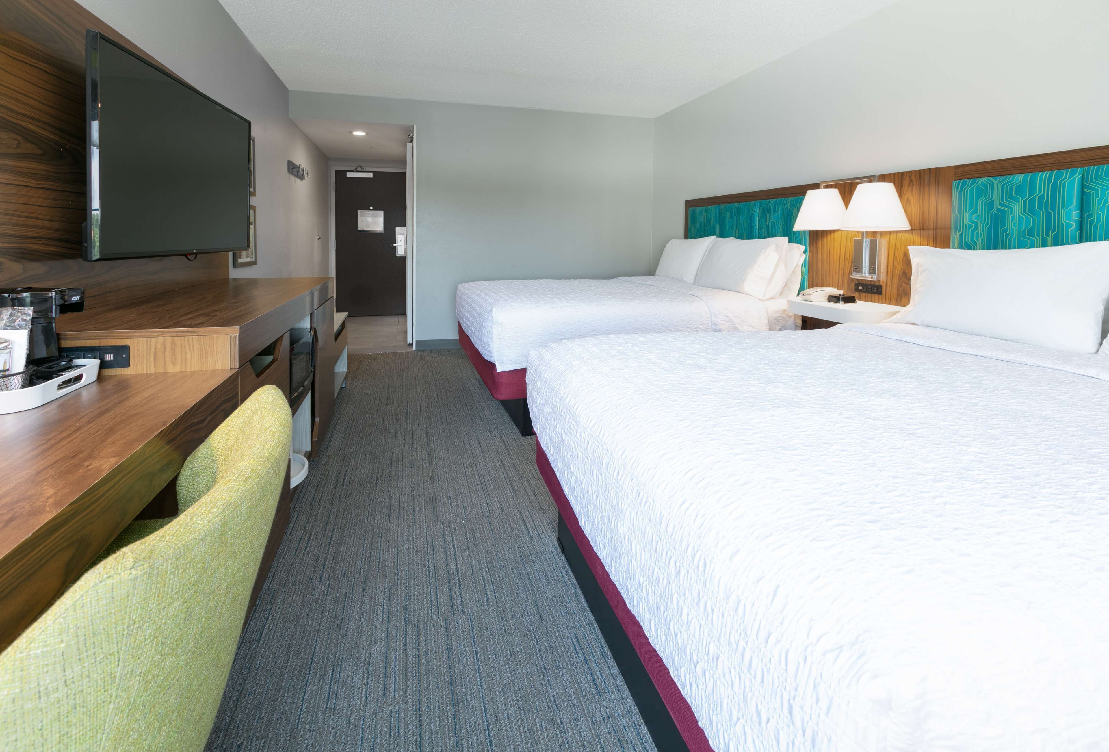 A hotel room with two beds, a desk with a TV, and a chair.