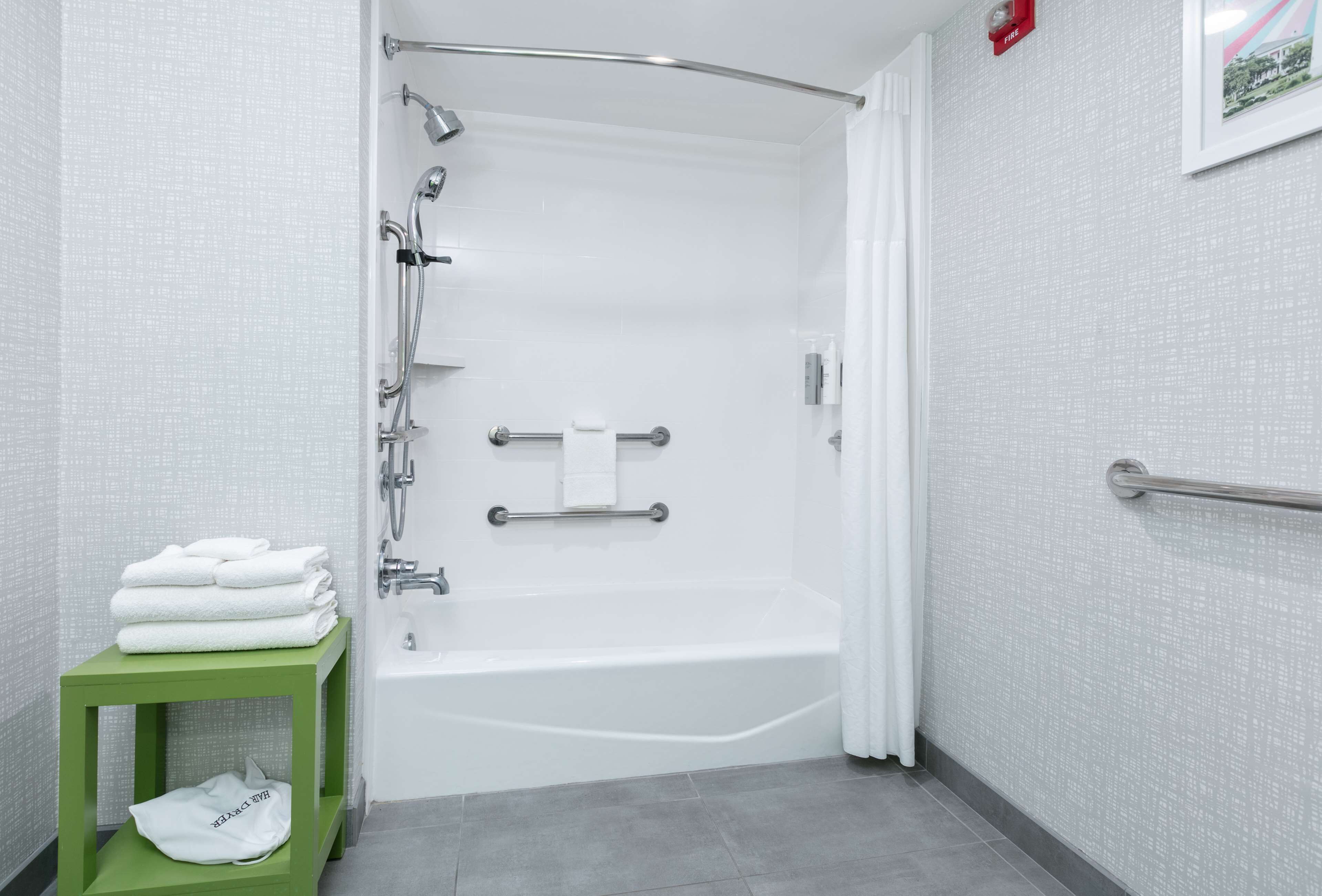 A modern bathroom with a white bathtub, a green stool, and a towel rack.