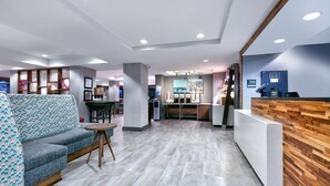 A modern hotel lobby with a reception desk, seating area, and a bar. - Hampton Inn Biloxi (Biloxi)