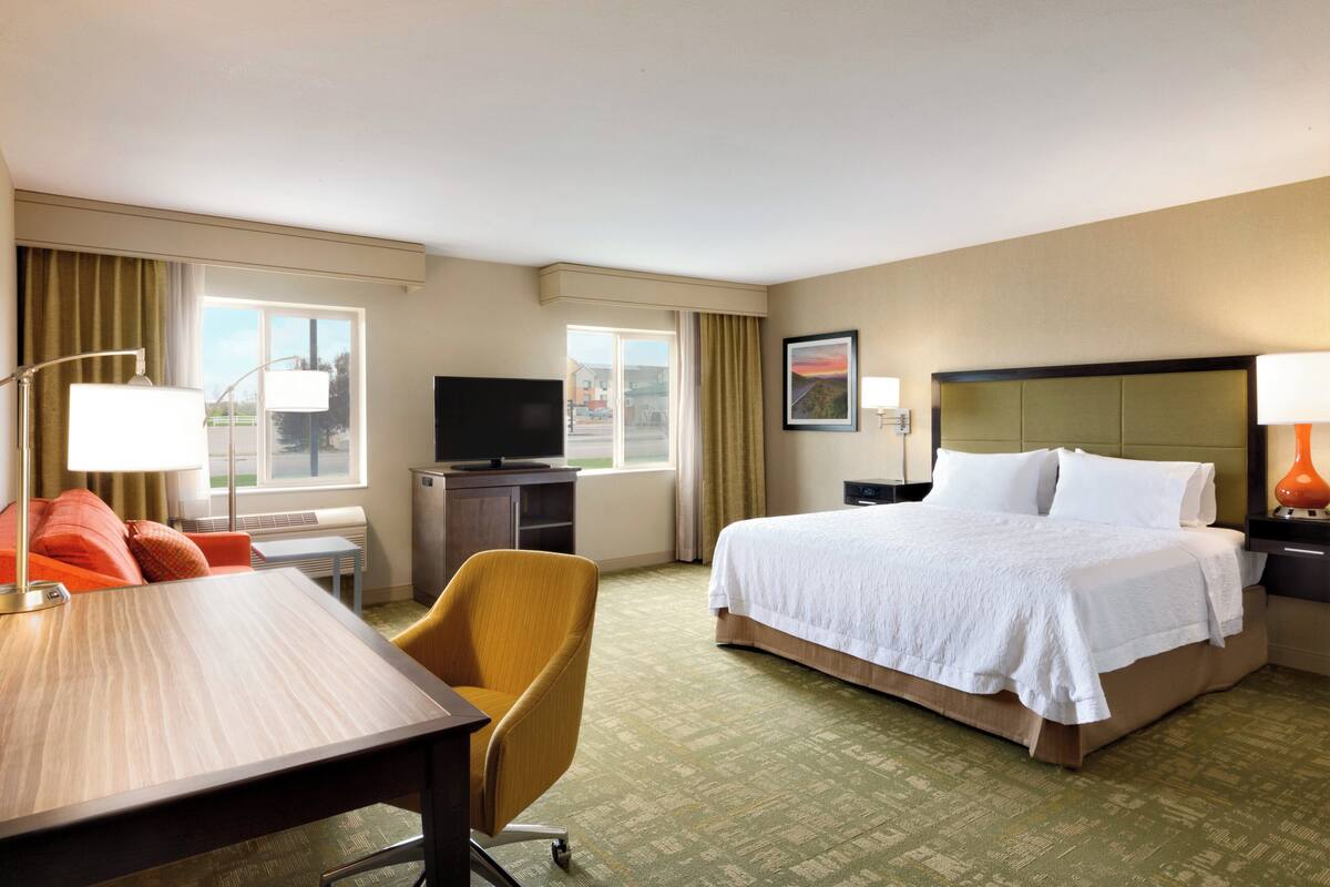 A hotel room with a bed, a desk, a chair, a television, and a window with curtains.