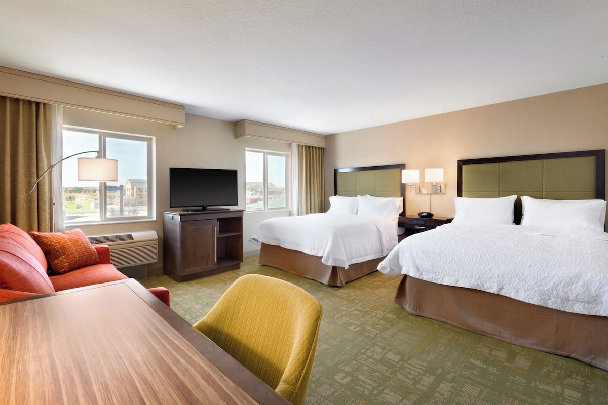 A hotel room with two beds, a TV, a desk, and a chair.