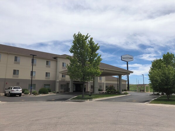 A hotel with a covered entrance, a sign indicating 'Summit Suites', and a parking lot with a white car.