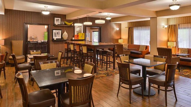Un vestíbulo de hotel con varias zonas de estar, mesas y sillas, una zona de bar y una recepción.