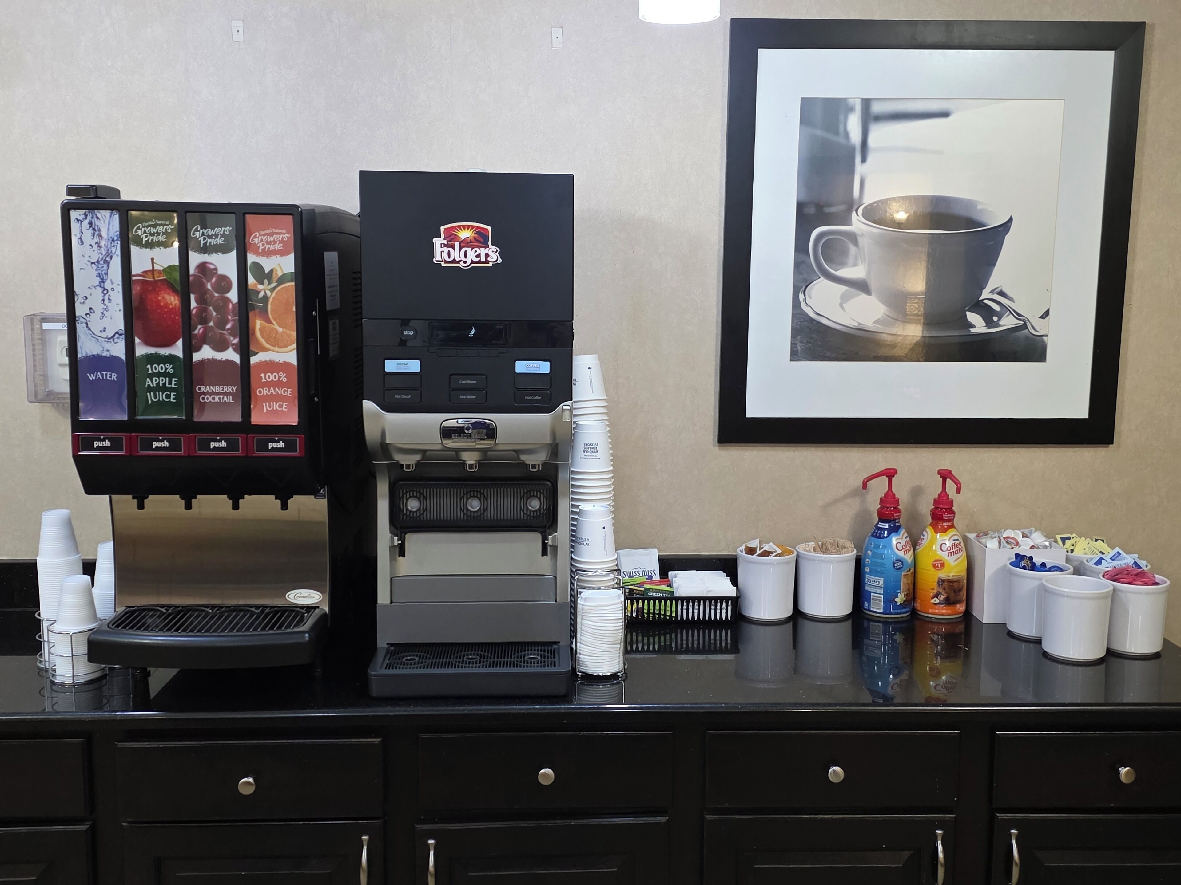 A coffee machine with a touchscreen menu, a framed picture of a cup of coffee, and various coffee and tea products on the counter.