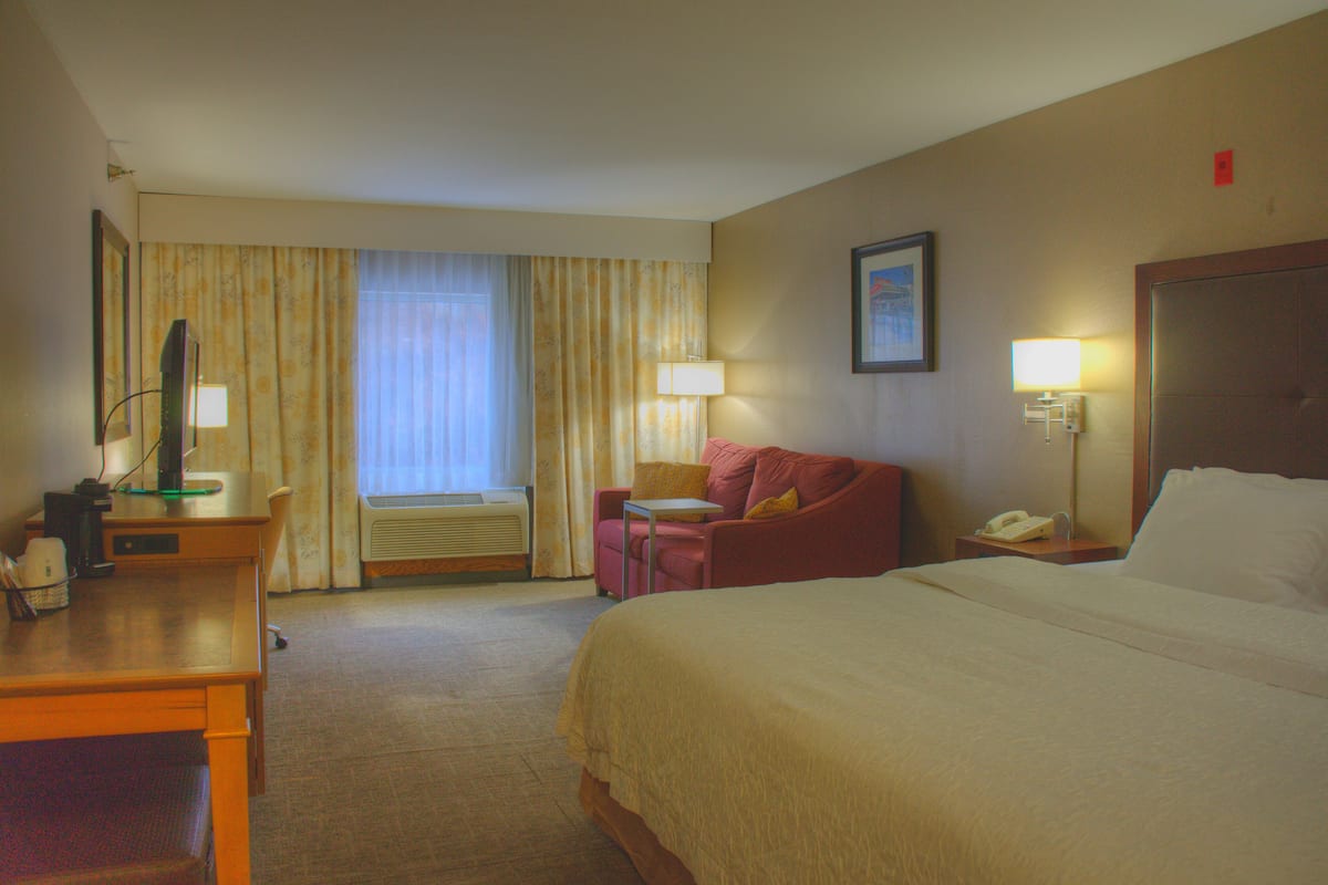 Habitación de hotel con cama, escritorio, silla, mesa, lámpara y teléfono.