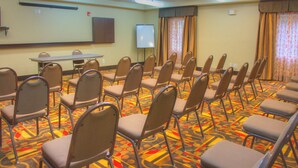 Un salón de conferencias con filas de sillas, una pizarra y una pantalla para proyector.