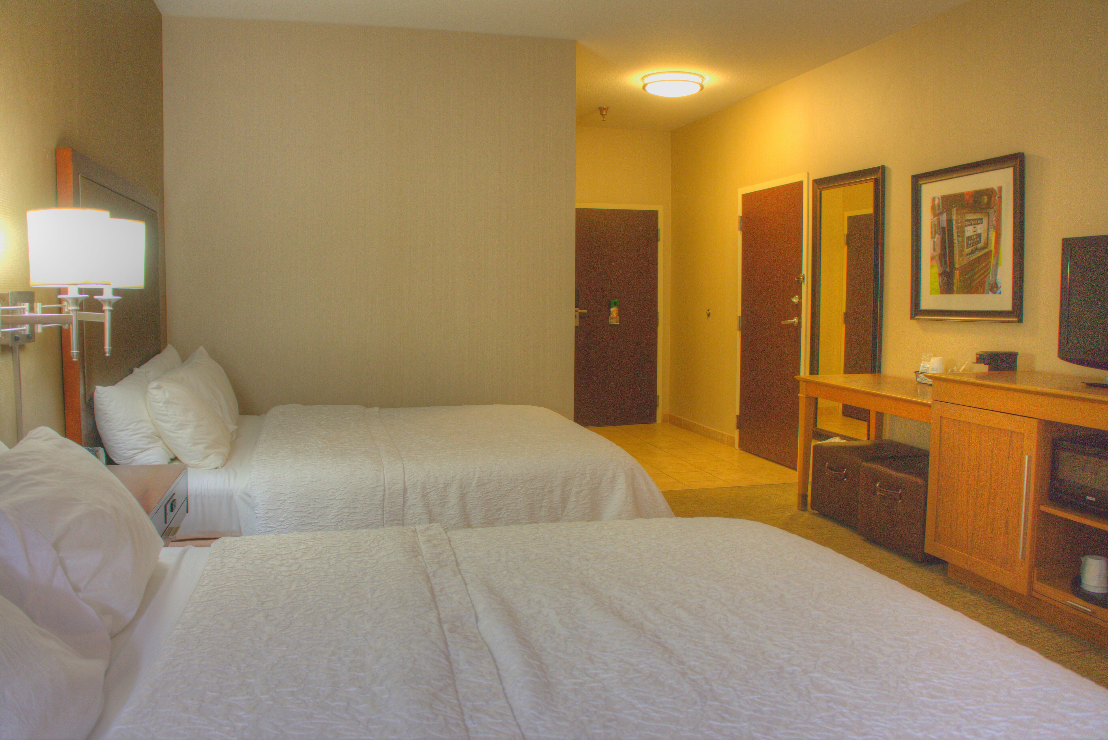 Habitación de hotel con dos camas, un escritorio con televisor y un espejo.