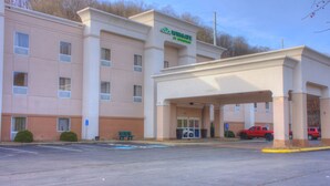 Un hotel de varios pisos con un acceso cubierto, un estacionamiento y una camioneta roja estacionada afuera.