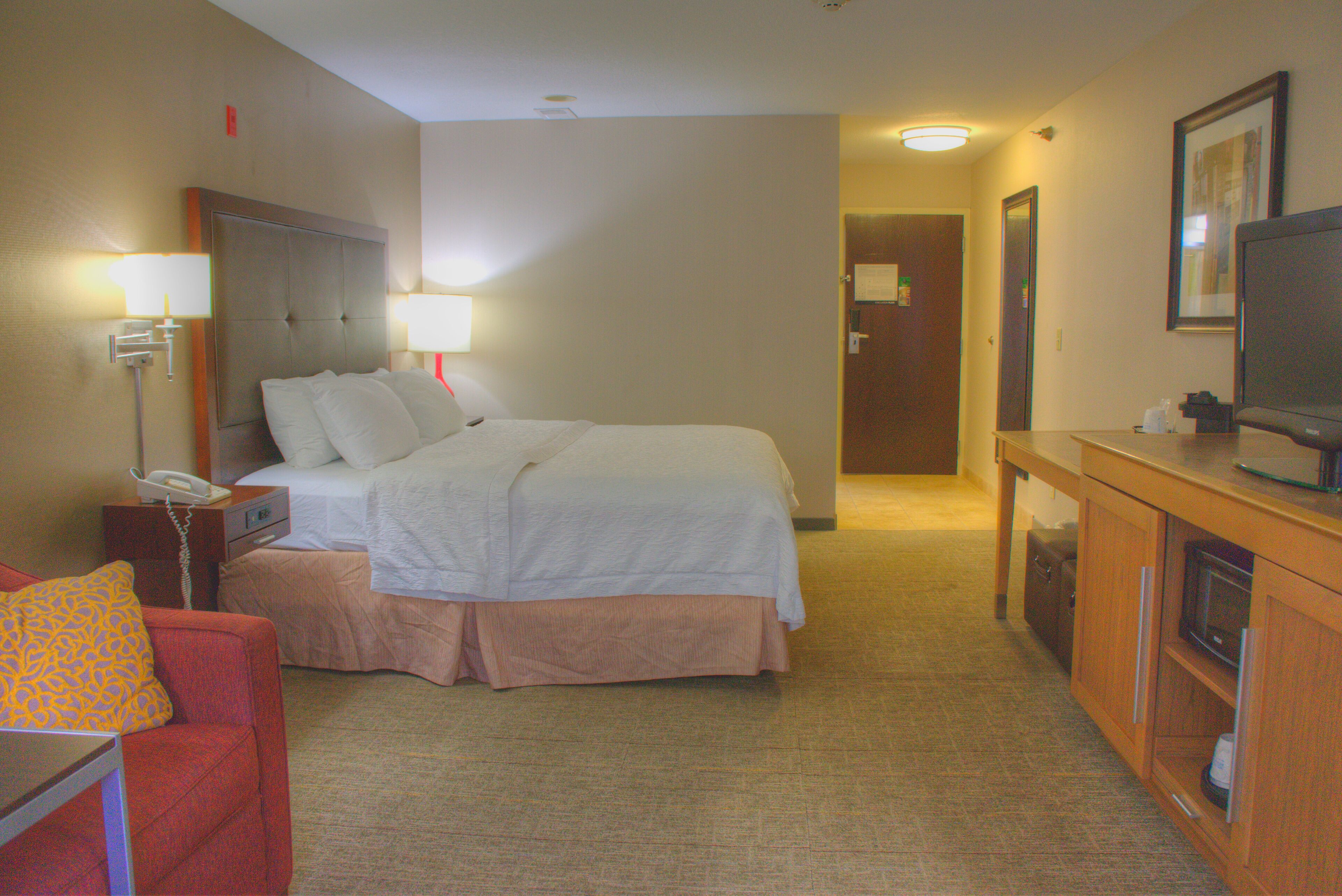 Quarto de hotel com cama, escrivaninha, telefone, televisão e armário.