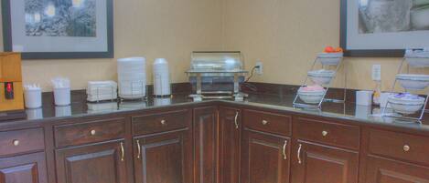 A kitchen area with a buffet setup, including a glass display case and various food items.
