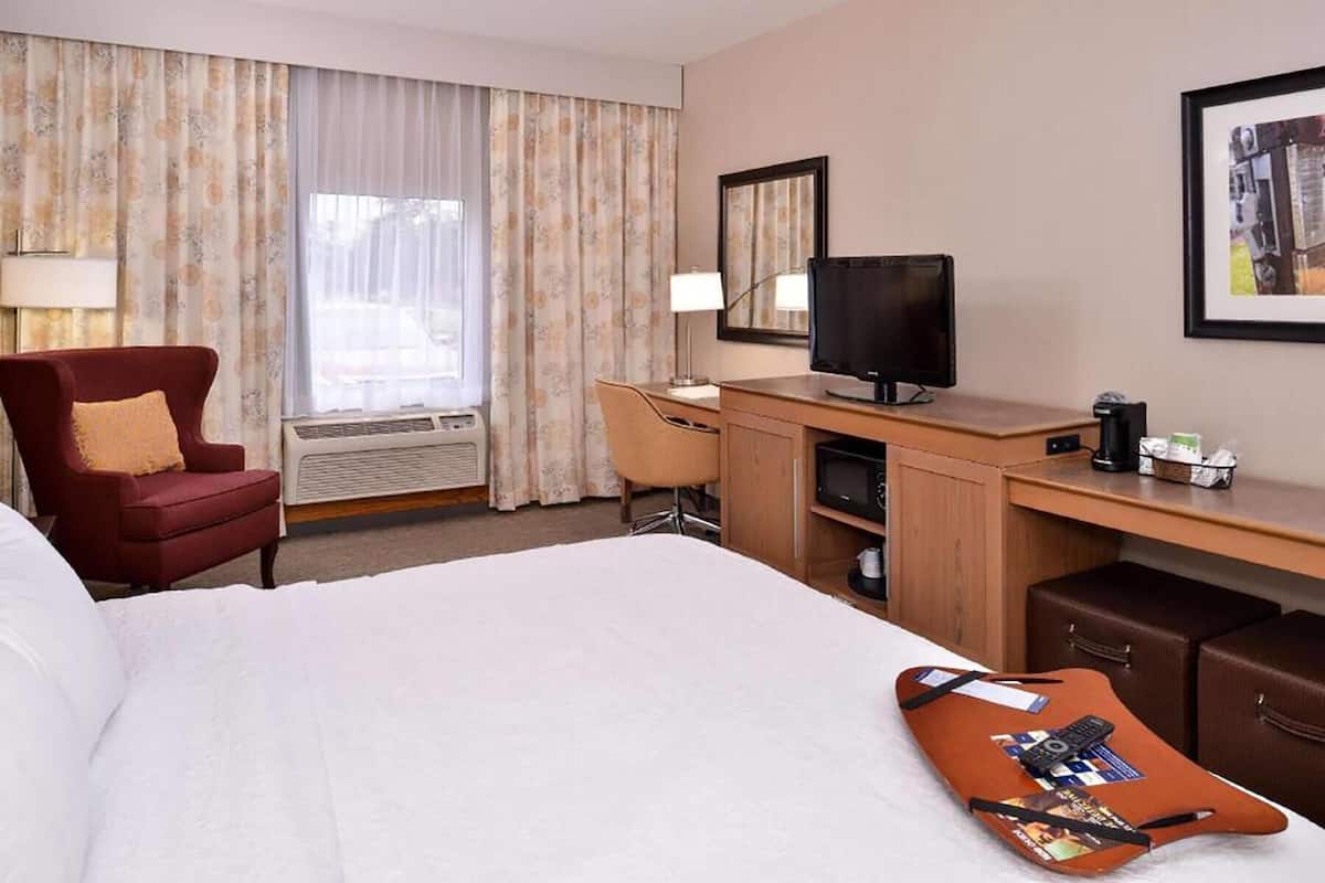 Una habitación de hotel con cama, escritorio, televisión, una silla y ventana con cortinas.