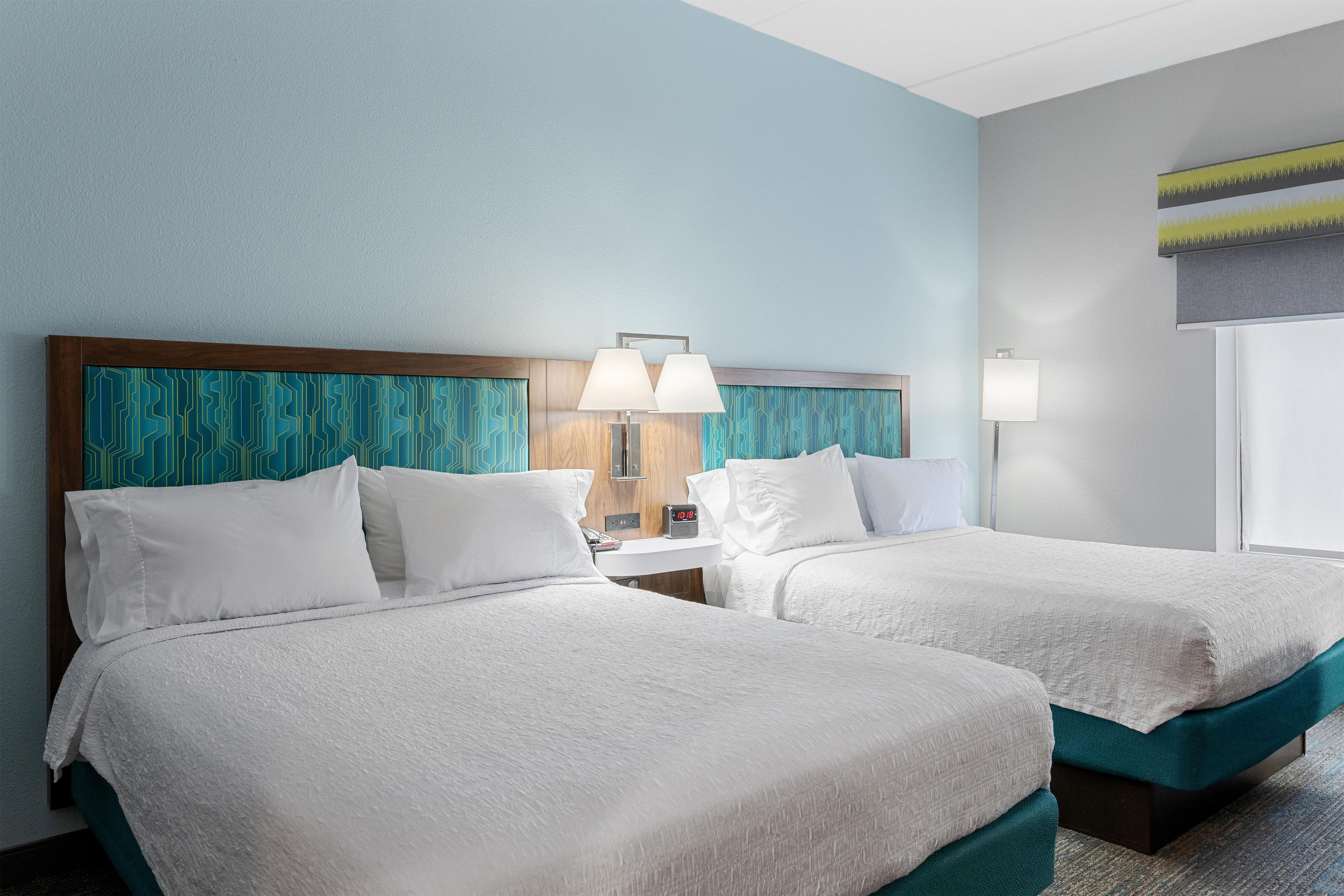 Une chambre d’hôtel avec deux lits, une table de chevet, une lampe et une fenêtre donnant sur un beau paysage.
