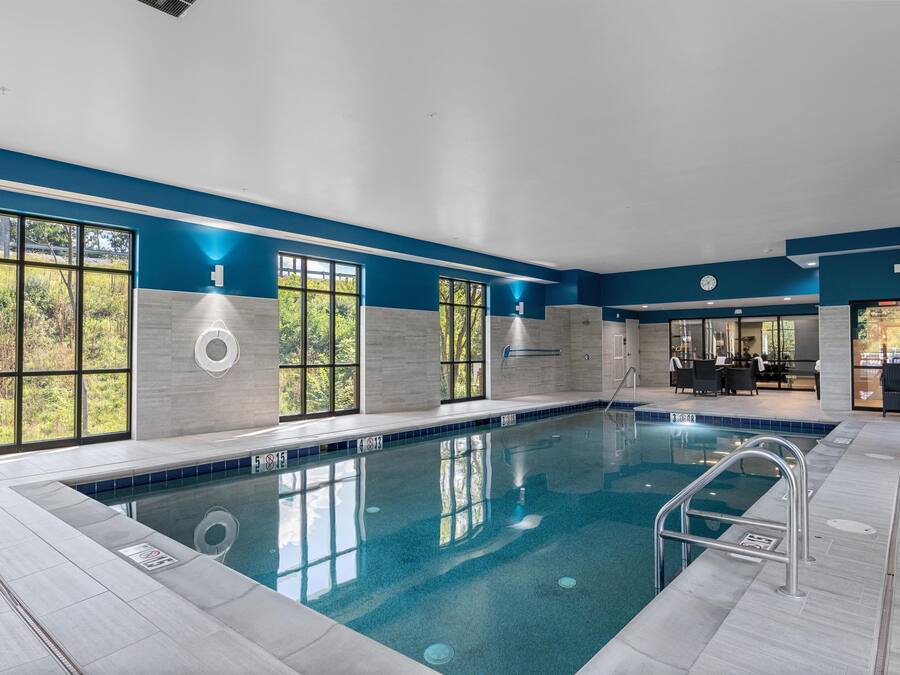 Una amplia piscina interior con agua cristalina y azul, rodeada de paredes con grandes ventanales que ofrecen vistas a zonas verdes.