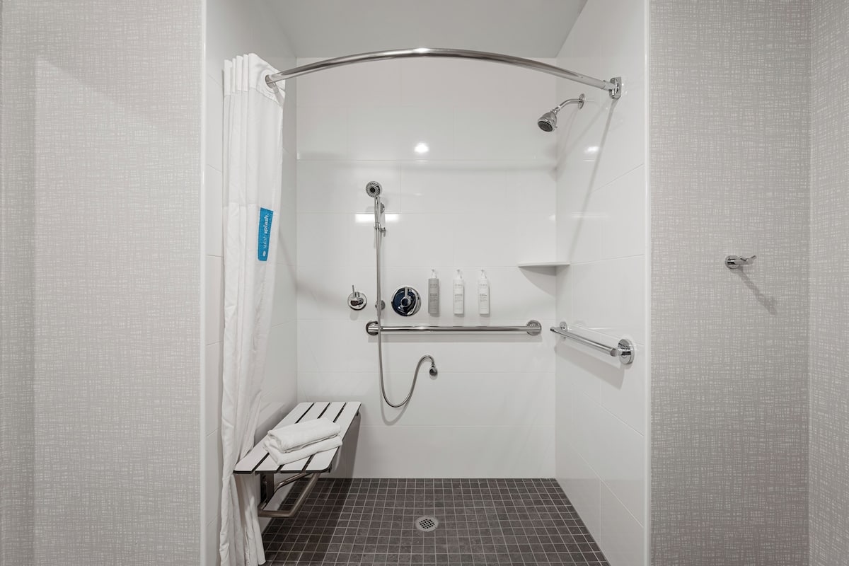 Eine bodenebene Dusche mit Haltegriff, Sitzbank und Ablage für Pflegeprodukte.