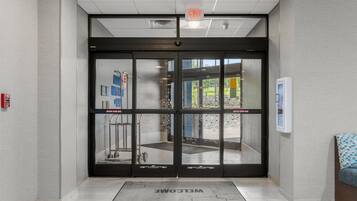 A modern entrance with a glass door, a welcome mat, and a fire alarm on the wall.