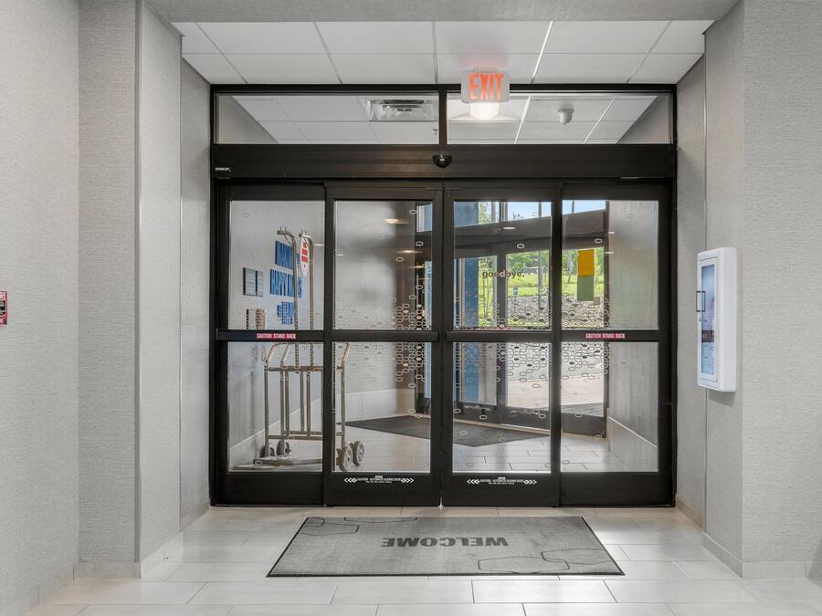A modern entrance with a glass door, a welcome mat, and a fire alarm on the wall.