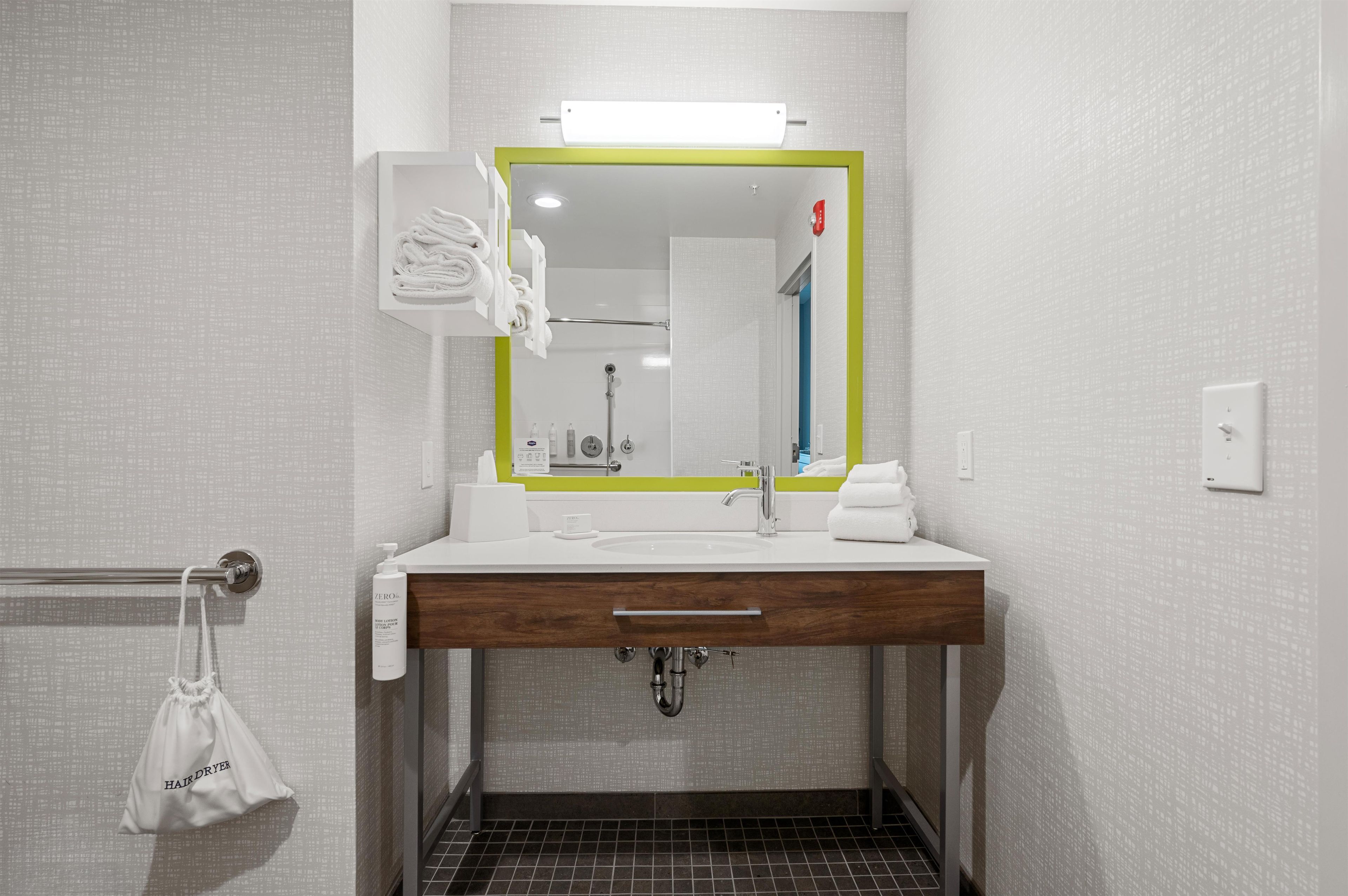 Un baño con un lavabo blanco, un espejo con marco verde, un perchero y una bolsa para secador de pelo.