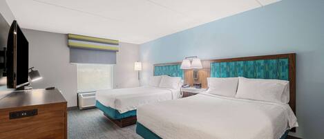 A hotel room with two beds, a desk with a TV, and a window with blinds.