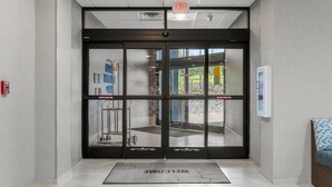 A modern entrance with glass doors, a welcome mat, and a fire extinguisher on the wall.