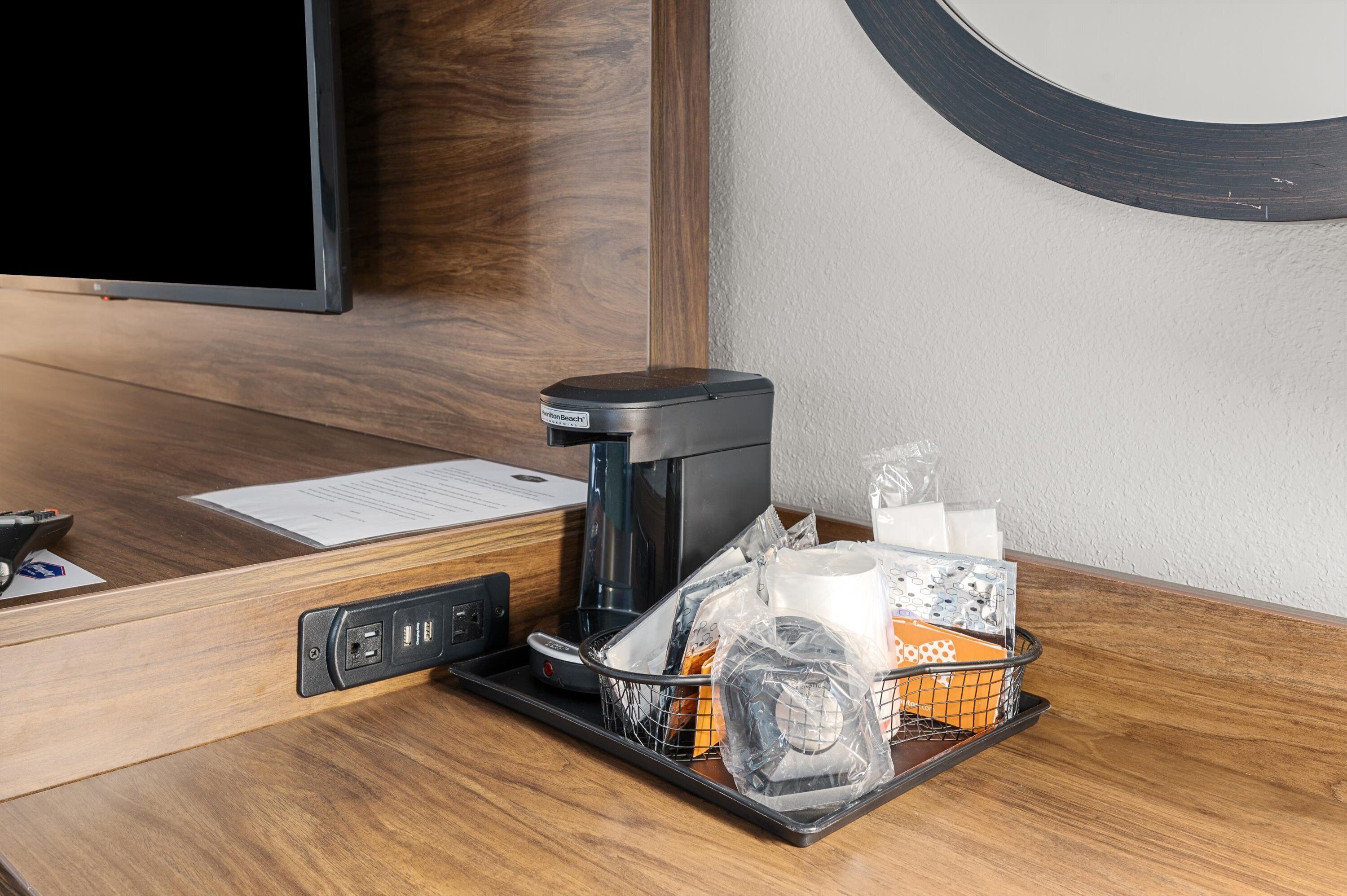 A hotel room with a coffee maker, a tray with toiletries, a remote control, and a television.