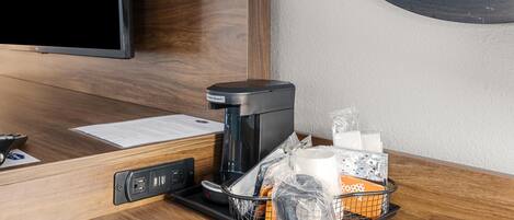 A hotel room with a coffee maker, a tray with toiletries, a remote control, and a television.