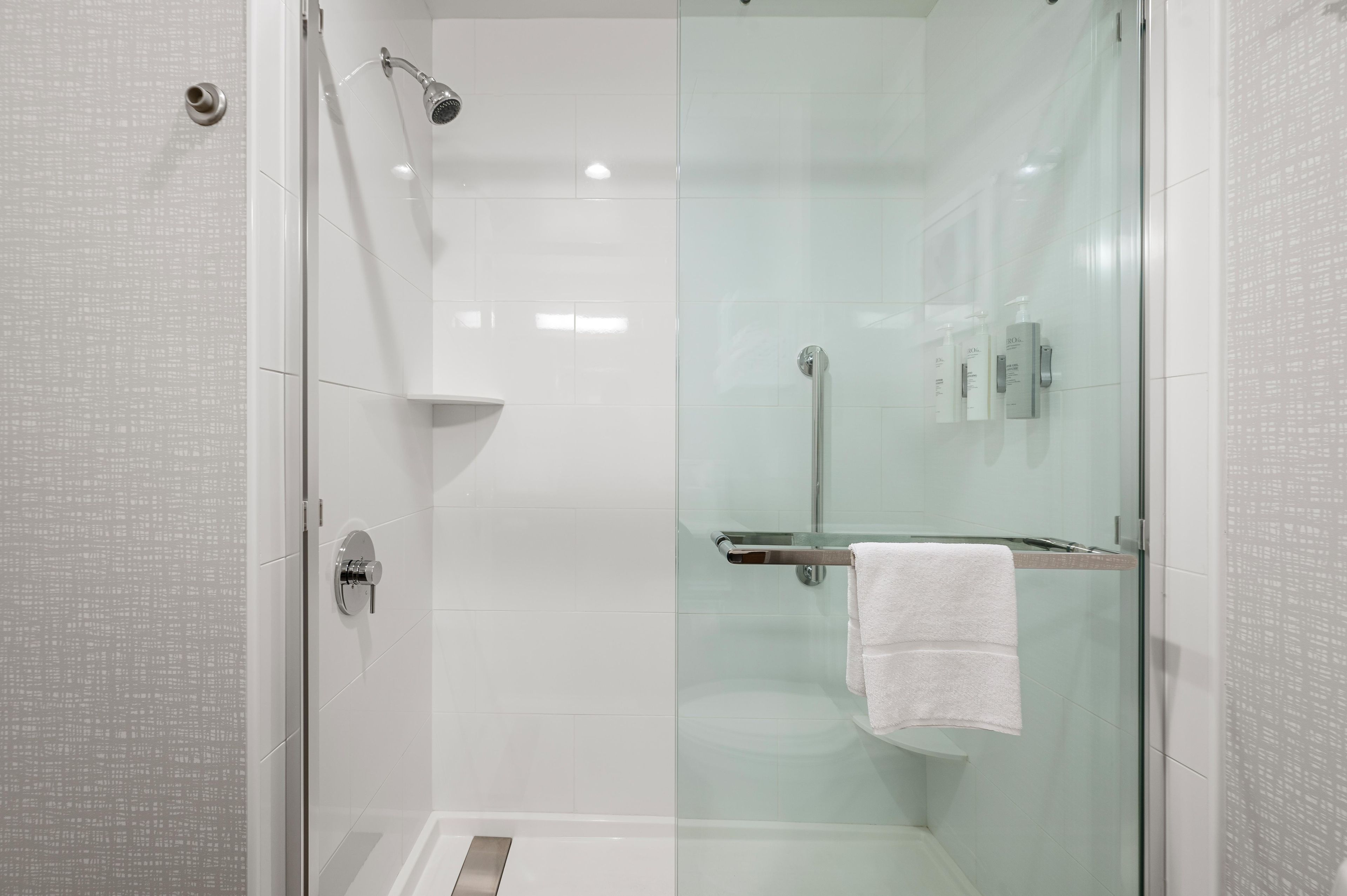 Une douche moderne dotée d’une porte en verre, d’un pommeau de douche à main et d’un porte-serviettes avec une serviette blanche.
