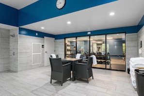 A modern indoor space with a dining area, a clock, and a view into a gym area. - Hampton Inn Front Royal (Front Royal)