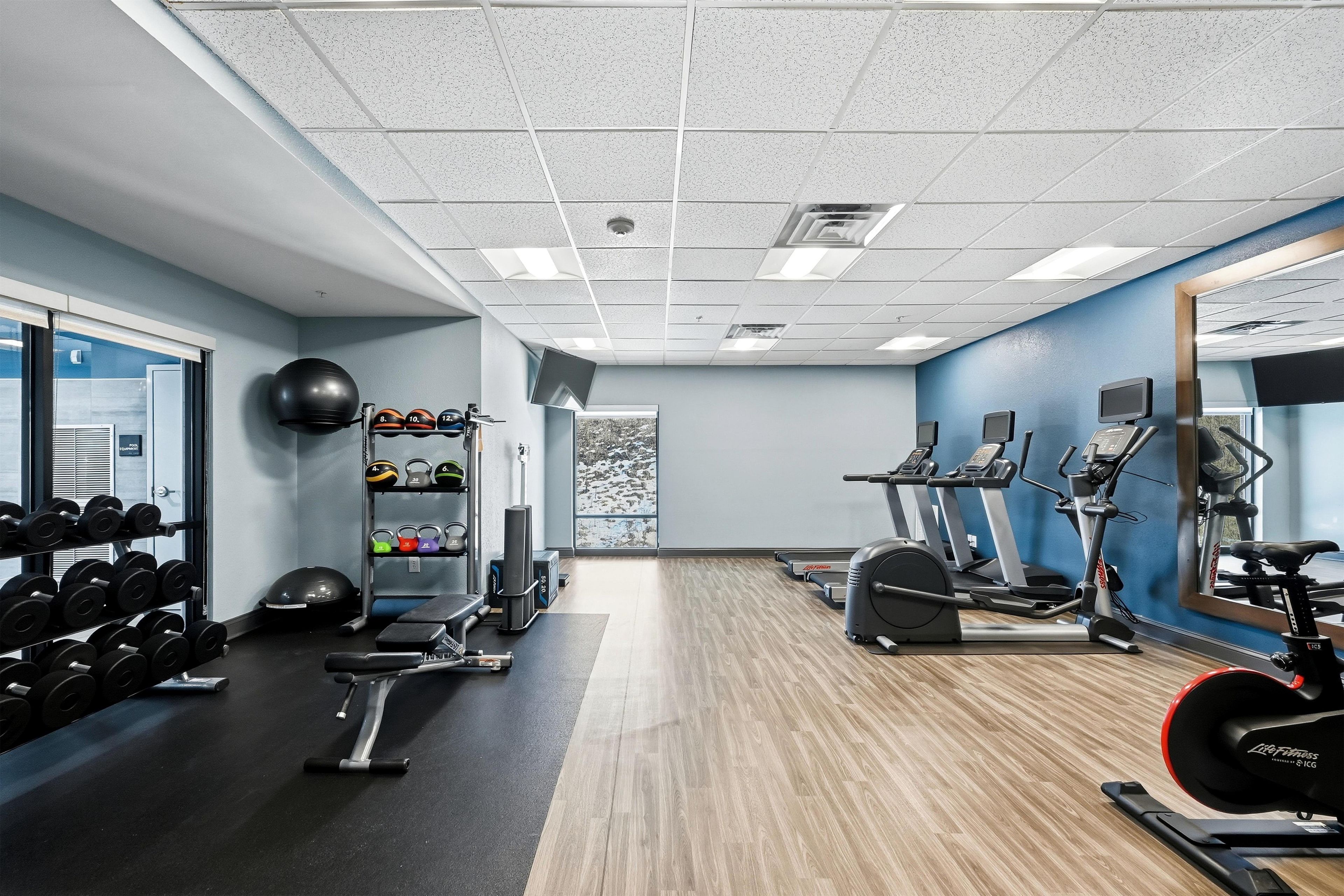 Une salle de sport équipée de matériel d’exercice, de supports pour les poids et d’un miroir.