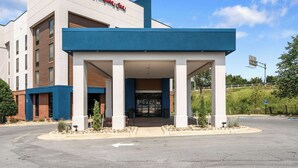 A modern hotel entrance with a covered waiting area, a clear sky, and a landscaped driveway.