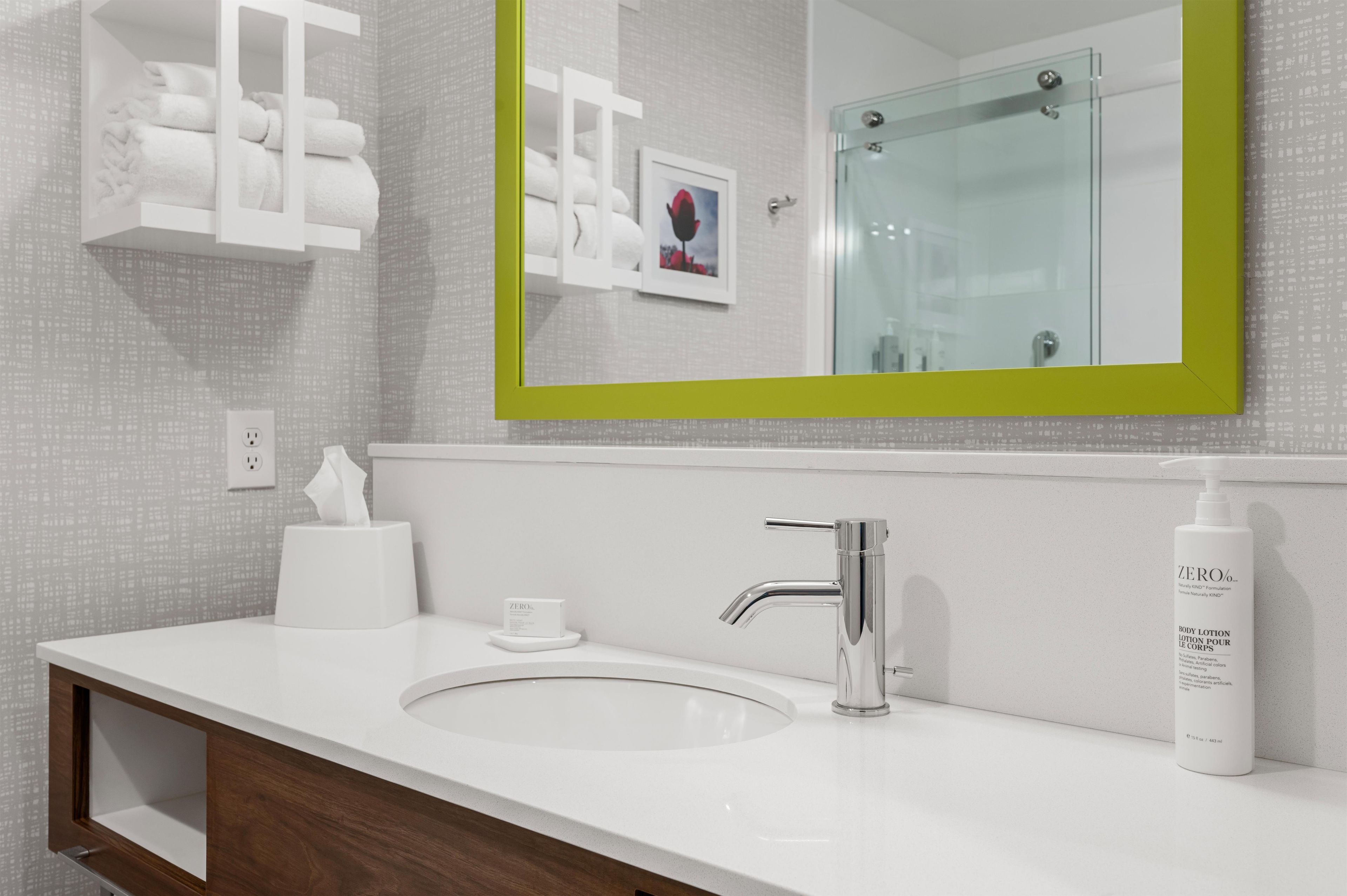 A modern bathroom with a white sink, chrome faucet, and a green-framed mirror.