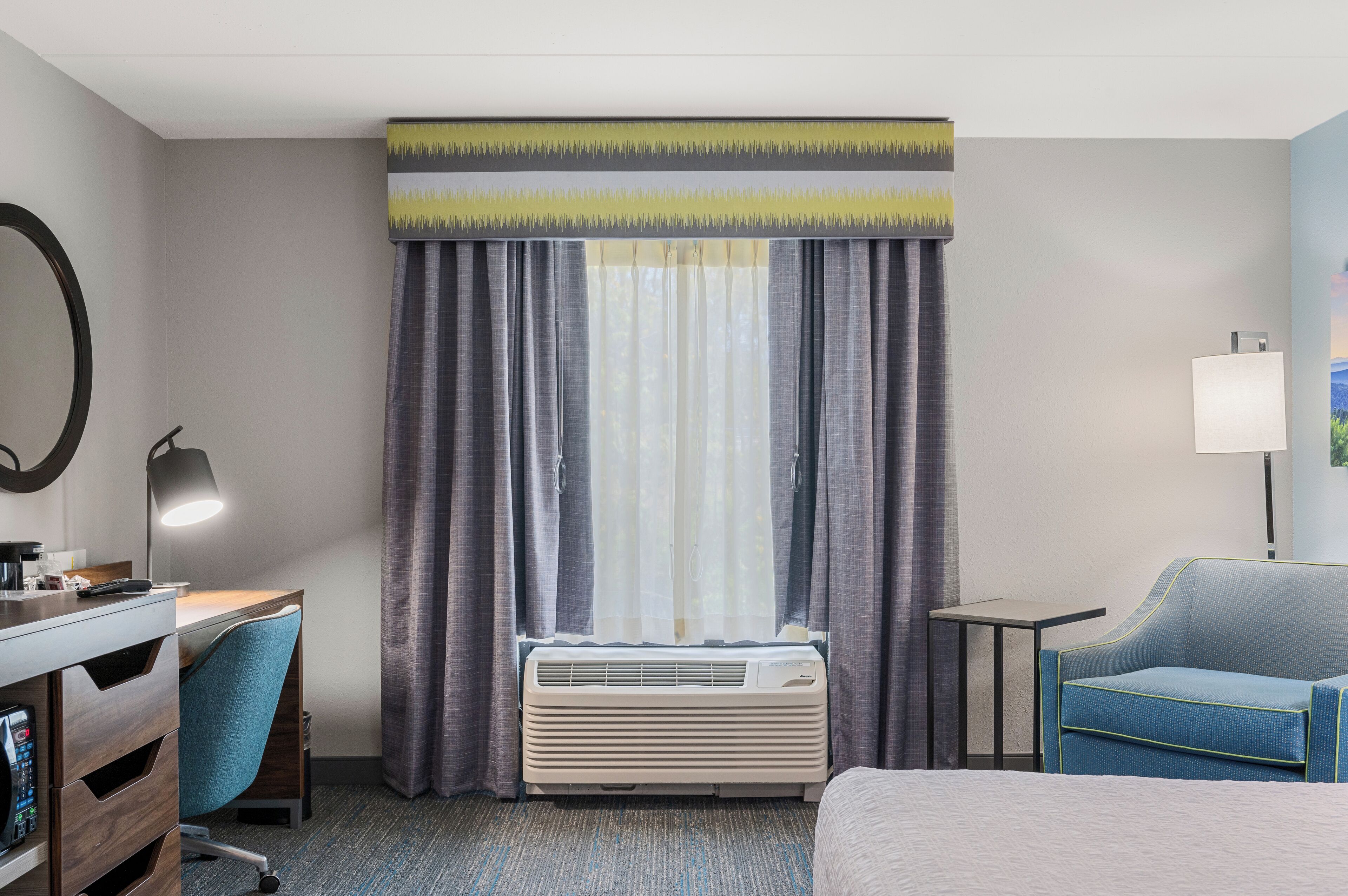 A hotel room with a desk, chair, air conditioner, and a bed.