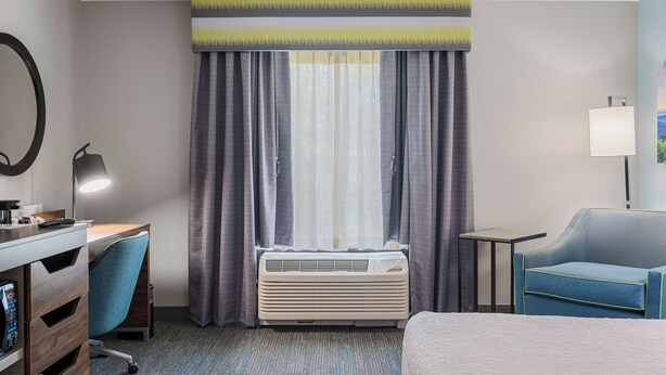 A hotel room with a desk, chair, air conditioner, and a bed.
