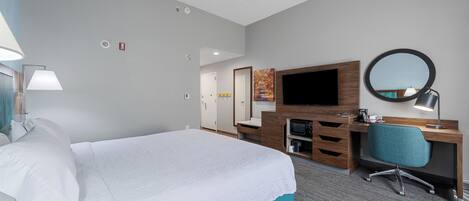 Habitación de hotel con una cama grande, un escritorio con silla, televisión y espejo.