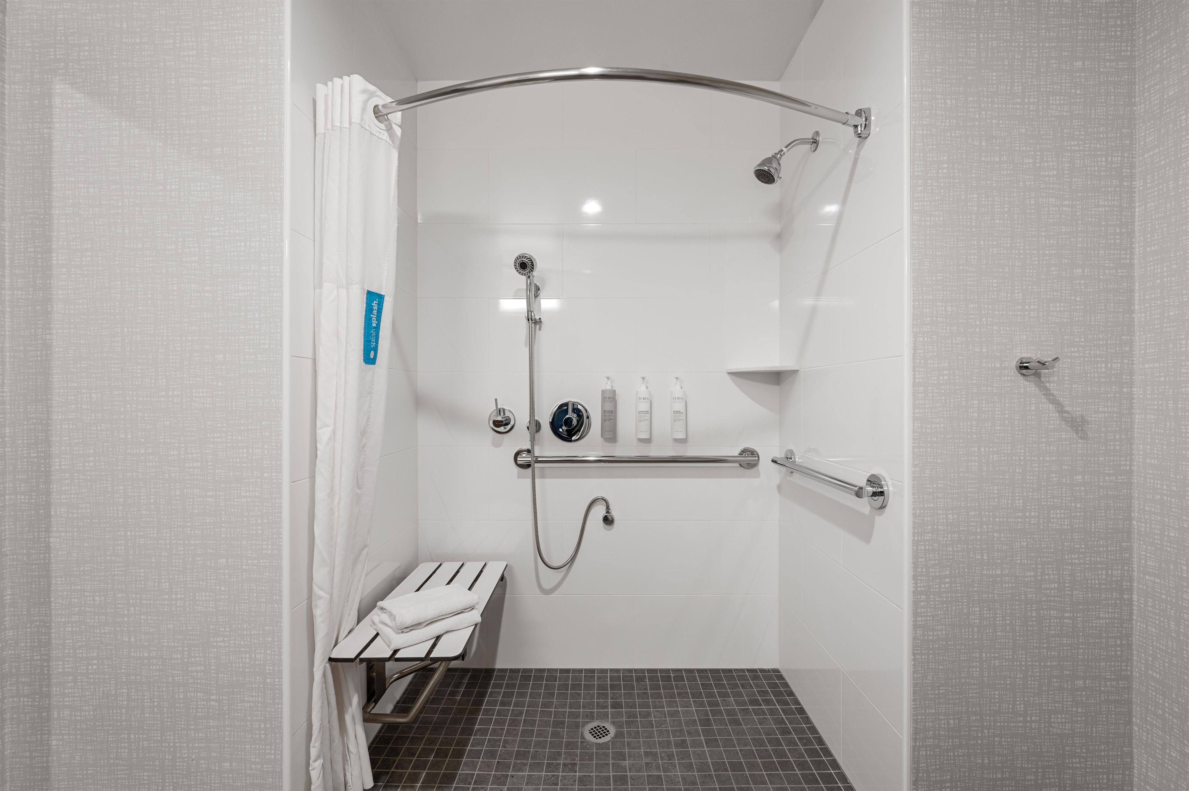Ein Duschbereich mit Haltegriff, Handbrause und am Wand befestigtem Wasserhahn.